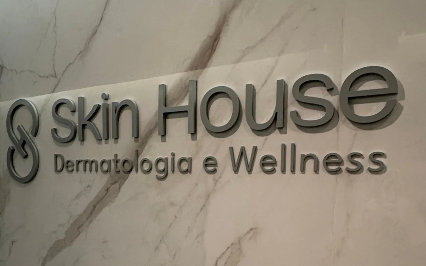 A marca Skin House aplicada em relevo sobre a parede de mármore da recepção